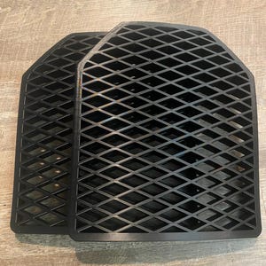 May include: Two black, rectangular panels with a diamond-shaped grid pattern. The panels have a slightly curved top edge and are designed to fit together. The items are made of a solid, matte black material.