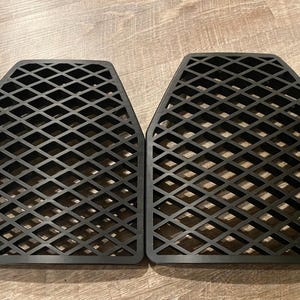 May include: Two black, diamond-patterned, rectangular objects with rounded corners. The objects have a grid-like design, and are placed side-by-side on a wooden surface. The objects appear to be made of a durable material.