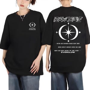 May include: Black short-sleeved t-shirt with a white graphic on the front and back. The front graphic includes a compass design and the text "EVERGLOW". The back features "RE:CODE" and a compass design with city names. A casual, unisex tee.
