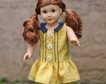 May include: A doll with red hair in pigtails wearing a yellow dress with a blue collar and white daisy buttons. The doll is wearing blue sandals and standing on a wooden surface.