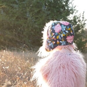 May include: A young person wearing a pink fuzzy jacket and a floral patterned hat. The hat has a dark blue background with pink, yellow, and green flowers.