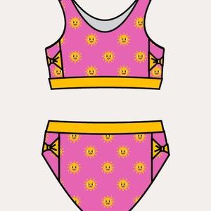 May include: A two-piece swimsuit set featuring a pink background with a repeating pattern of smiling yellow suns. The top has wide straps and the bottoms have yellow accents.