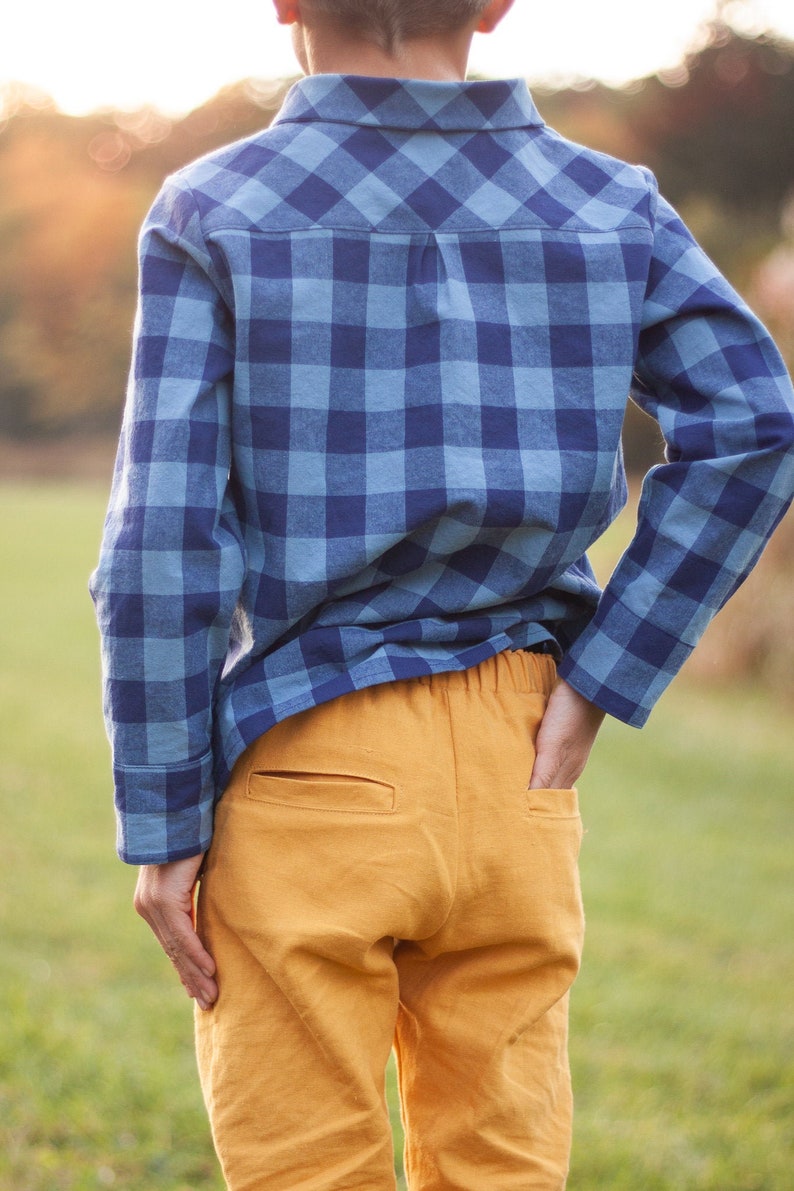 Op de afbeelding: Een jongen draagt een lang mouw overhemd met blauw-witte ruitjes en een mosterdgele broek.