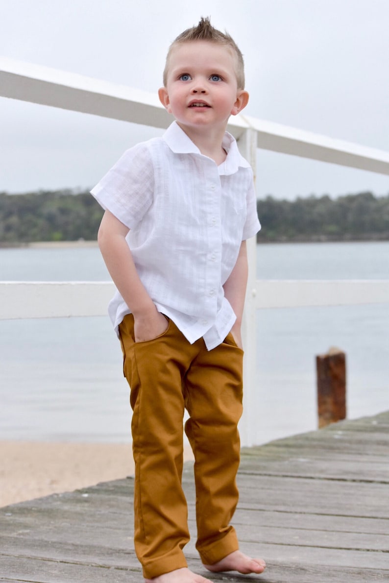 Op de afbeelding: Een jonge jongen in een wit linnen shirt en een bruine broek staat op een houten pier. Hij kijkt omhoog en naar rechts.