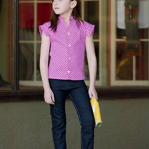 May include: A young person wearing a pink and white gingham button-up shirt with short sleeves and rolled up blue jeans. They are wearing brown sandals and holding a yellow and white patterned fabric.