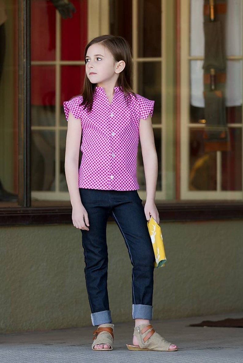 May include: A young person wearing a pink and white gingham button-up shirt with short sleeves and rolled up blue jeans. They are wearing brown sandals and holding a yellow and white patterned fabric.