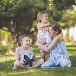 Pu&ograve; includere: Tre ragazze sono sedute in un'area erbosa. La ragazza al centro tiene un libro. La ragazza a destra abbraccia la ragazza a sinistra. Tutte e tre le ragazze sorridono.