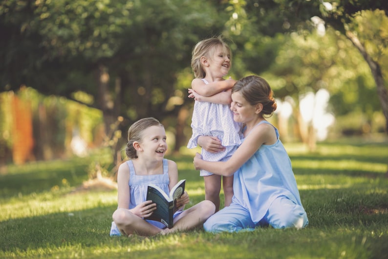 Pu&ograve; includere: Tre ragazze sono sedute in un'area erbosa. La ragazza al centro tiene un libro. La ragazza a destra abbraccia la ragazza a sinistra. Tutte e tre le ragazze sorridono.