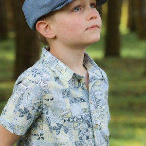 May include: A young person wearing a light blue patterned shirt and a denim newsboy cap. The person is looking up and to the right.