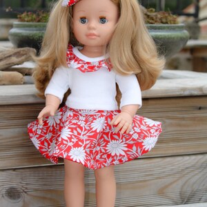 May include: A doll with long blonde hair wearing a white shirt with a red and white ruffled collar, a red and white floral skirt, and blue denim sneakers.