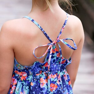 May include: A blue and pink floral print dress with a tie back. The dress has a ruffled hem and a sleeveless design.