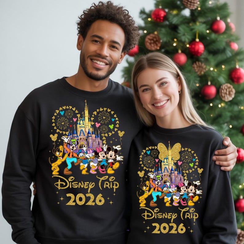 May include: Black sweatshirts with a Disney Trip 2026 design. The design features a castle, fireworks, and Disney characters. The sweatshirts are worn by a smiling couple in front of a Christmas tree.