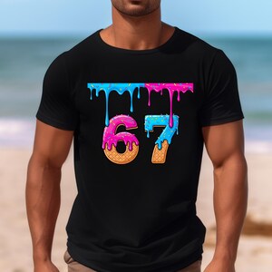 May include: Black t-shirt featuring the number "67" in a playful, cartoonish style. The numbers are designed to resemble donuts, with pink and blue icing dripping down. The shirt has a crew neck and short sleeves.
