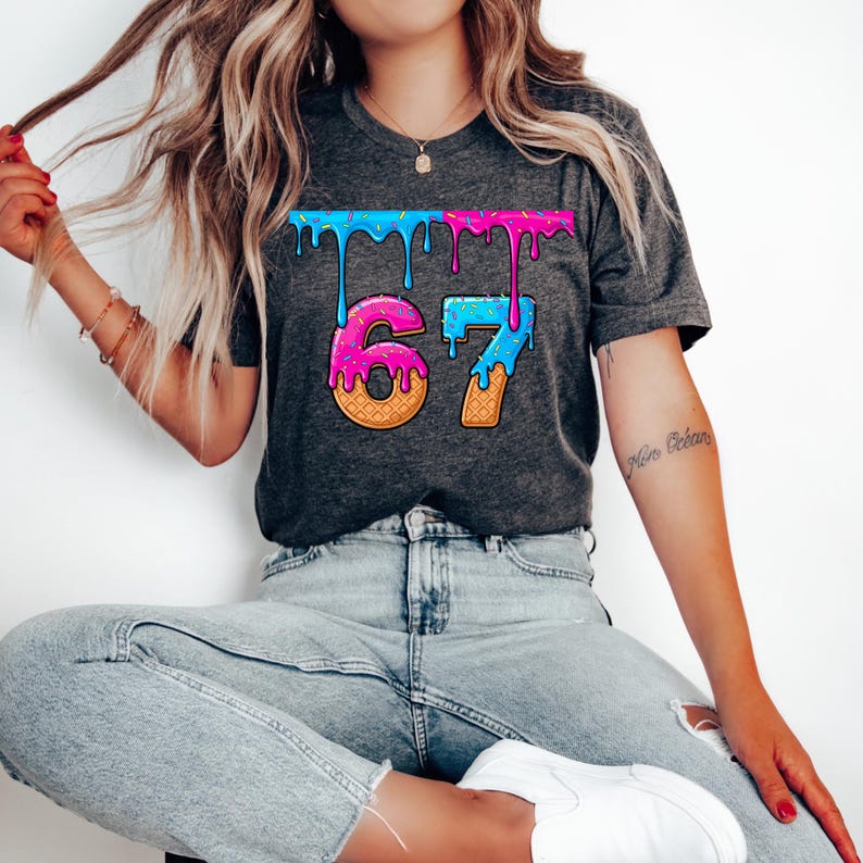 May include: Dark gray t-shirt featuring the number "67" in a playful, ice cream-themed design. The numbers are styled as ice cream cones with pink and blue dripping frosting. The shirt has a classic crew neck and short sleeves.