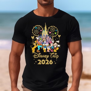 May include: Black t-shirt featuring a colorful graphic of Disney characters in front of a castle, with fireworks and balloons. The text "Disney Trip 2026" is written in gold glitter font.