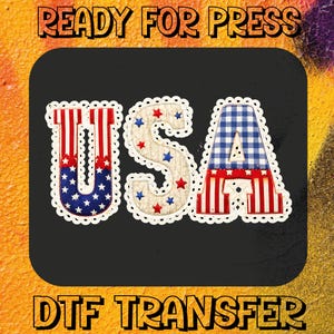 May include: A patriotic USA design in red, white, and blue. The letters are decorated with stars and stripes, and the design is framed with a white scalloped edge. The text "READY FOR PRESS" and "DTF TRANSFER" are also included.