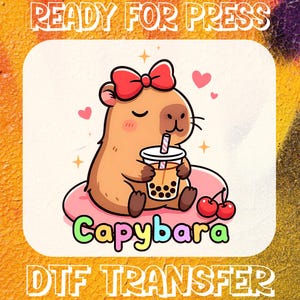 May include: DTF transfer with a cartoon capybara wearing a red bow, enjoying boba tea. The image includes the text "Capybara" and "DTF TRANSFER" on a colourful background. The words "READY FOR PRESS" are also visible.