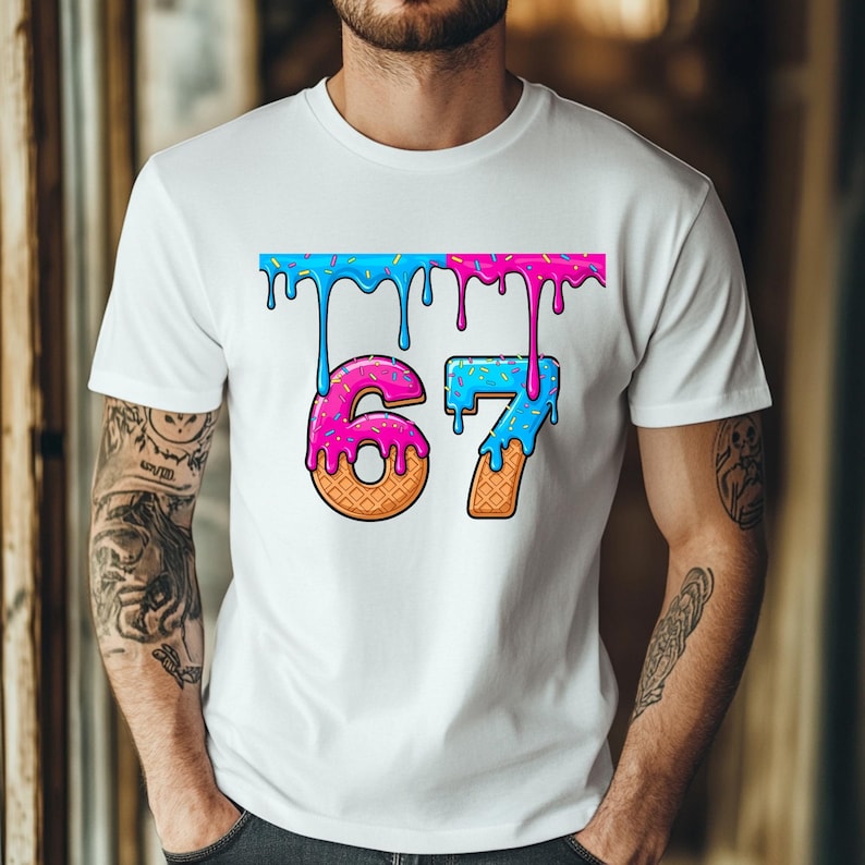 May include: White t-shirt featuring a colorful graphic of the number "67". The numbers are designed to look like ice cream cones with dripping blue and pink frosting, and a sprinkle border.