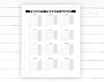 May include: A white framed calendar print for the year Twenty Twenty-Eight. The calendar features a grid layout with each month displayed in a separate box. The text "TWENTY TWENTY-EIGHT" is printed at the top in a bold, black font.
