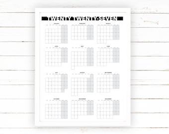 May include: A white framed calendar print for the year "TWENTY TWENTY-SEVEN". The calendar features a grid layout with each month displayed, and the weekends are highlighted in gray. The print is on a white wooden background.