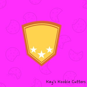 May include: A yellow shield-shaped cookie cutter with three white stars at the bottom, set against a pink background with cookie outlines. The text "Kay's Kookie Cutters" is at the bottom.