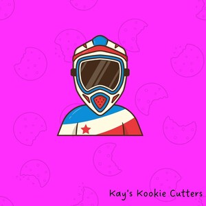May include: A cartoon illustration of a motocross racer wearing a helmet with a red, white, and blue design. The racer's uniform features a star. The background is pink with cookie shapes. The text "Kay's Kookie Cutters" is at the bottom.