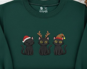 May include: A dark green sweatshirt with embroidered images of three black cats in festive hats. The cats are wearing a Santa hat, reindeer antlers, and an elf hat. The sweatshirt has a crew neck and long sleeves.