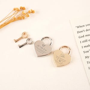 May include: Heart-shaped padlocks and keys in silver and gold tones. The padlocks are engraved with text, including names and a date. The keys have heart-shaped keyholes. The items are arranged on a light-colored surface.