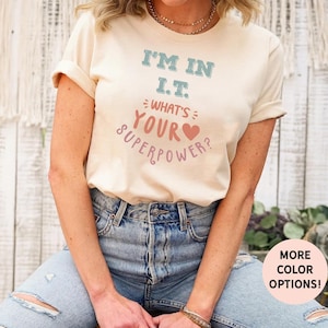 May include: A light beige t-shirt with the text "I'm in I.T. What's your superpower?" in a colourful font with a pink heart.
