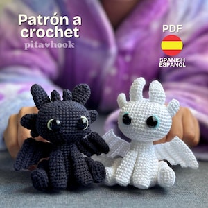 Puede incluir: Dos figuras de dragones de ganchillo, una negra y otra blanca, con ojos grandes y expresivos. El dragón negro tiene alas oscuras, mientras que el dragón blanco tiene alas blancas. La imagen incluye el texto "Patrón a crochet" y "PDF Spanish Español".