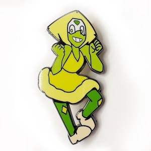 May include: A green and yellow enamel pin featuring a cartoon character with a green dress and a large green gem on her forehead. The character is smiling and has her arms raised in the air.