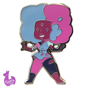 May include: A metal enamel pin featuring a cartoon character with dark red skin, three eyes, and large, voluminous hair split into light blue and bright pink sections. The character wears a light blue and pink top with dark blue and pink leggings.