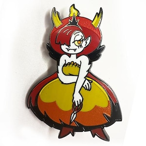 May include: A red and yellow enamel pin featuring a cartoon character with red hair, horns, and a yellow dress. The character is holding a pair of scissors.