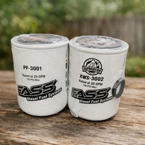 May include: Two white FASS Diesel Fuel Systems filters. One is labeled PF-3001, rated at 25 GPM, 100 PSI Max. The other is XWS-3002, a water separator, also rated at 25 GPM, 100 PSI Max. Both have the FASS logo.