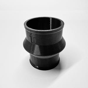 Op de afbeelding: Een zwart, 3D-geprint cilindrisch object met een pijlsymbool. Het object heeft een uitlopend middengedeelte en een gladde, matte afwerking. Het object is waarschijnlijk een connector of adapter.
