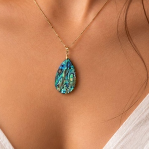 May include: A teardrop-shaped pendant featuring iridescent blue and green abalone shell inlay, suspended from a delicate gold-tone chain. The pendant displays a natural, multi-coloured mosaic pattern with shimmering highlights across its surface.