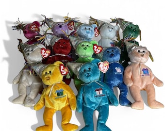 May include: A collection of 12 plush beanie baby bears wearing party hats. Each bear is a different color and has a different month of the year embroidered on its chest. The bears are all sitting on a white surface.
