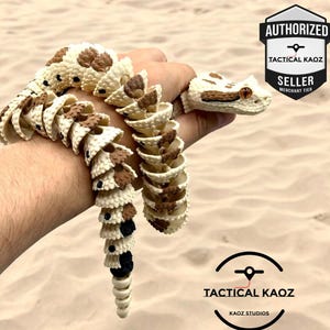 May include: An articulated, segmented toy snake featuring a cream-coloured base with brown and black patterned markings. The snake has a detailed head with visible eyes and a flexible, jointed body structure that allows for movement and posing.
