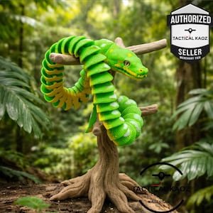 May include: A segmented, articulated green and yellow snake toy coiled around a brown textured branch. The snake features a bright green back with white spots and a yellow underside. A black and white shield logo reads AUTHORIZED TACTICAL KAOZ SELLER.