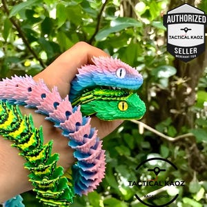 May include: Three colourful, articulated toy snakes are held in a hand. The top snake is pink and blue, the middle one is green and yellow, and the bottom one is green and yellow. The snakes have detailed scales and realistic eyes. The image includes the text "AUTHORIZED SELLER" and "TACTICAL KAOZ".
