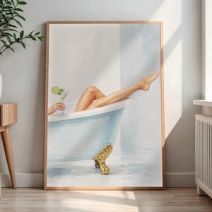 May include: A framed wall art print depicting a light blue clawfoot bathtub with gold-toned feet. A pair of legs extends from the tub, and a hand holds a clear stemmed glass containing a cocktail garnished with a green lime slice.