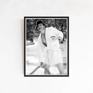 Op de afbeelding: Zwart-wit ingelijste print van een persoon in een witte badjas, korte broek en hoed, die een slang vasthoudt. De persoon staat in een besneeuwde omgeving, met bomen op de achtergrond. Medium shot.