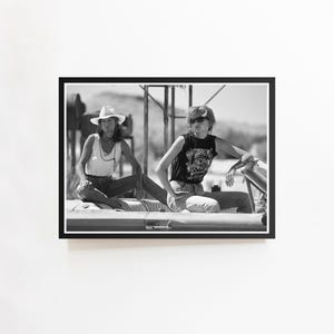 Puede incluir: Fotografía en blanco y negro de dos personas sentadas en el borde de un coche descapotable. Una persona lleva un sombrero de vaquero y la otra gafas de sol. Ambos visten ropa informal.