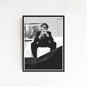 Könnte beinhalten: Schwarz-Weiß-Druck in einem Rahmen, der eine Person im Anzug beim Anzünden einer Zigarette zeigt. Der Druck hat einen weißen Rand und wird an einer weißen Wand angezeigt. Die Person sitzt auf einer weißen Oberfläche.