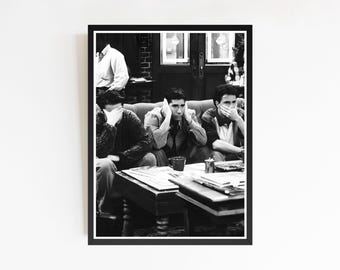 May include: Black and white framed print depicting a scene from the TV show "Friends." The image shows three men seated on a sofa, with one man standing in the background. A coffee table with books and a cup is in front of the sofa.