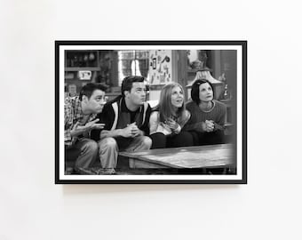 Op de afbeelding: Zwart-wit ingelijste print met vier mensen die op een bank zitten en omhoog kijken. De afbeelding is een still uit de televisieserie "Friends", in een woonkamer.