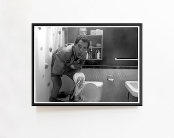 May include: Black and white framed print of a scene from a movie. A person is in a bathroom, looking surprised while holding toilet paper. The bathroom has a toilet, sink, and shower curtain.