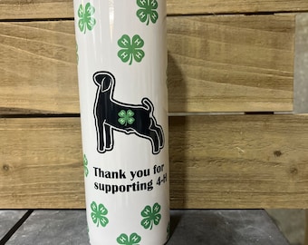 May include: A white cylindrical tumbler featuring a repeating pattern of green four-leaf clover 4-H logos. A black silhouette of a goat is centered on the front, also containing a green 4-H logo. The text Thank you for supporting 4-H is printed below.