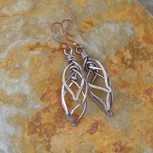 May include: A pair of silver wire earrings with a leaf design. The earrings are hanging from copper hooks.
