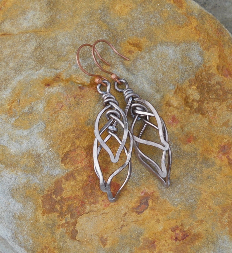 May include: A pair of silver wire earrings with a leaf design. The earrings are hanging from copper hooks.